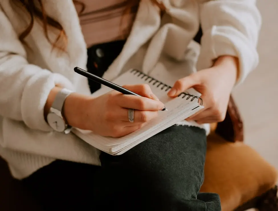 Hands writing in small spiral notebook on lap