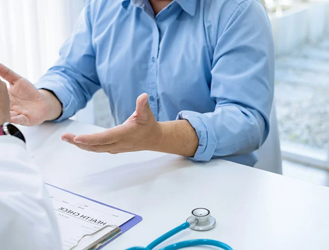 Patient gesturing during health consultation with stethoscope on desk