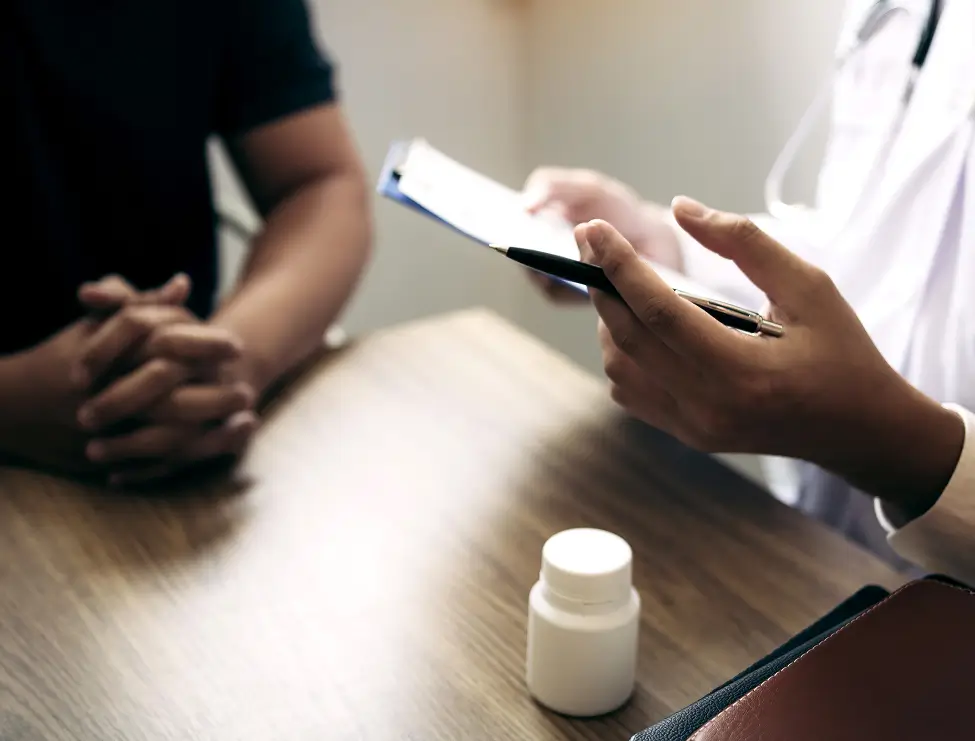 Medical professional discussing medication with patient at consultation table.