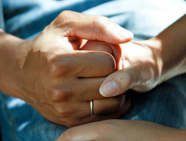 Two hands clasped in a comforting hold, one wearing a plain ring